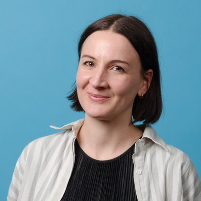 Anna Snowball standing in front of blue backgound, smiling.